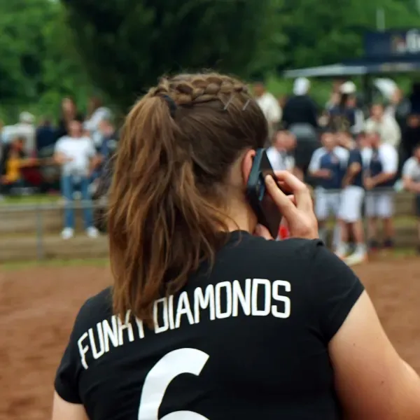 'FUNKY DIAMONDS'-Spielerin mit geflochtener Frisur und Pferdeschwanz in schwarzem Trikot und Rückennummer 6, telefoniert während eines Spiels.