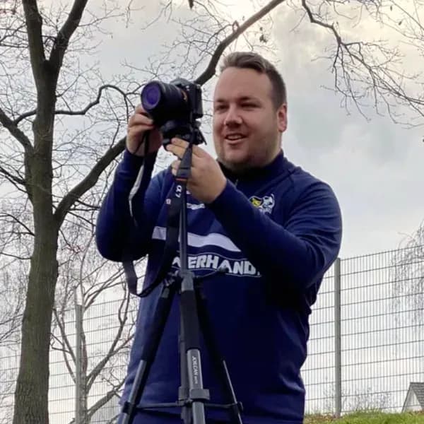 PR-Team-Mitglied der TSG Irlich in blau-weißem Vereinstrikot mit Kamera auf Stativ bei der Arbeit im Freien.