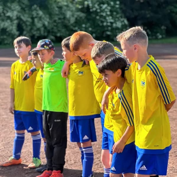 Jugend-Fußballmannschaft der TSG Irlich in gelb-blauen Trikots steht Arm in Arm auf dem Sportplatz